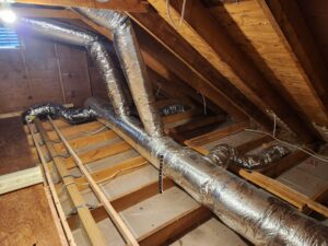 Insulated flexible HVAC ductwork running across attic ceiling joists with an insulation depth ruler installed before blown-in insulation.