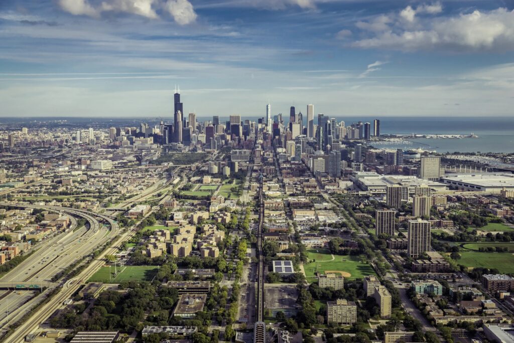 Aerial view of the Chicago skyline with Lake Michigan, expressway, and surrounding neighborhoods in the foreground.