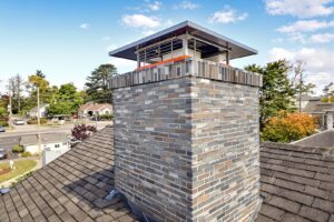 Rebuilt multi-color brick chimney with stainless steel chase cover and cap on an asphalt shingle roof.