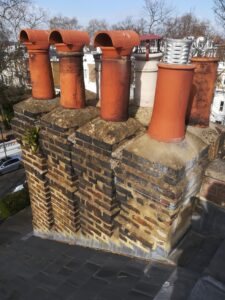 Multi-flue brick chimney stack topped with terracotta chimney pots and a metal spinning cowl on a slate roof